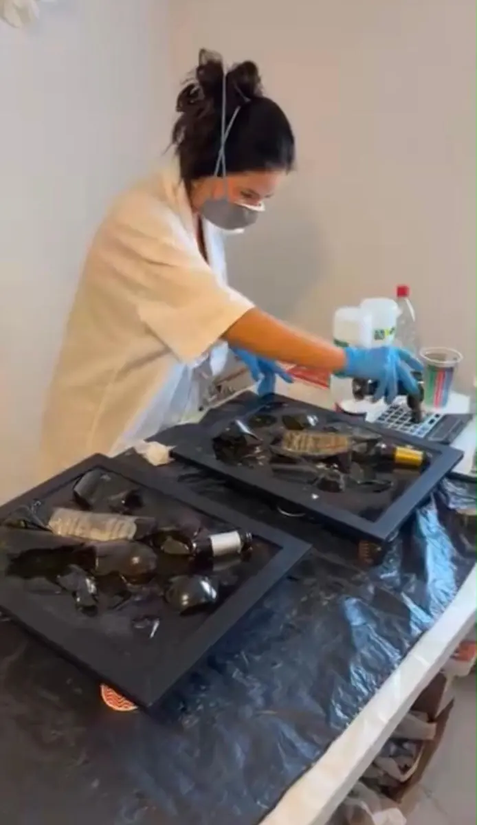 Amanda Berton, masque et gants, appliquant de la résine sur des éclats de verre dans son atelier